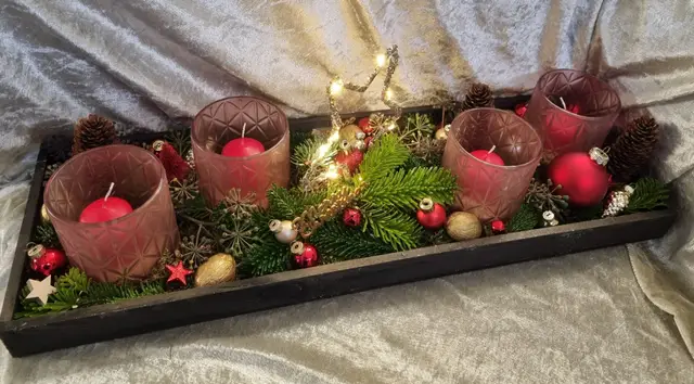 Dunkles Holztablett mit rosa Windlichtern, roten Kerzen, Kugeln und Lichterkette